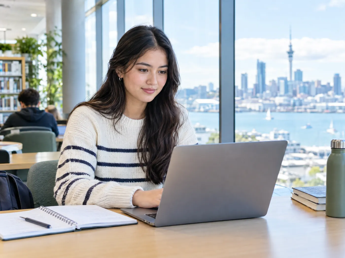 International student studying in a bright library overlooking Auckland Harbour and the Sky Tower